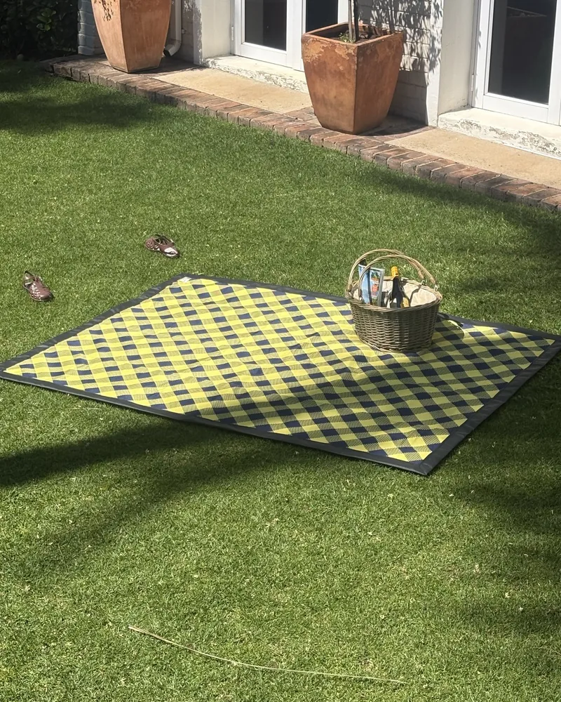 Yellow and navy checked picnic blanket with a picnic basket on a garden lawn